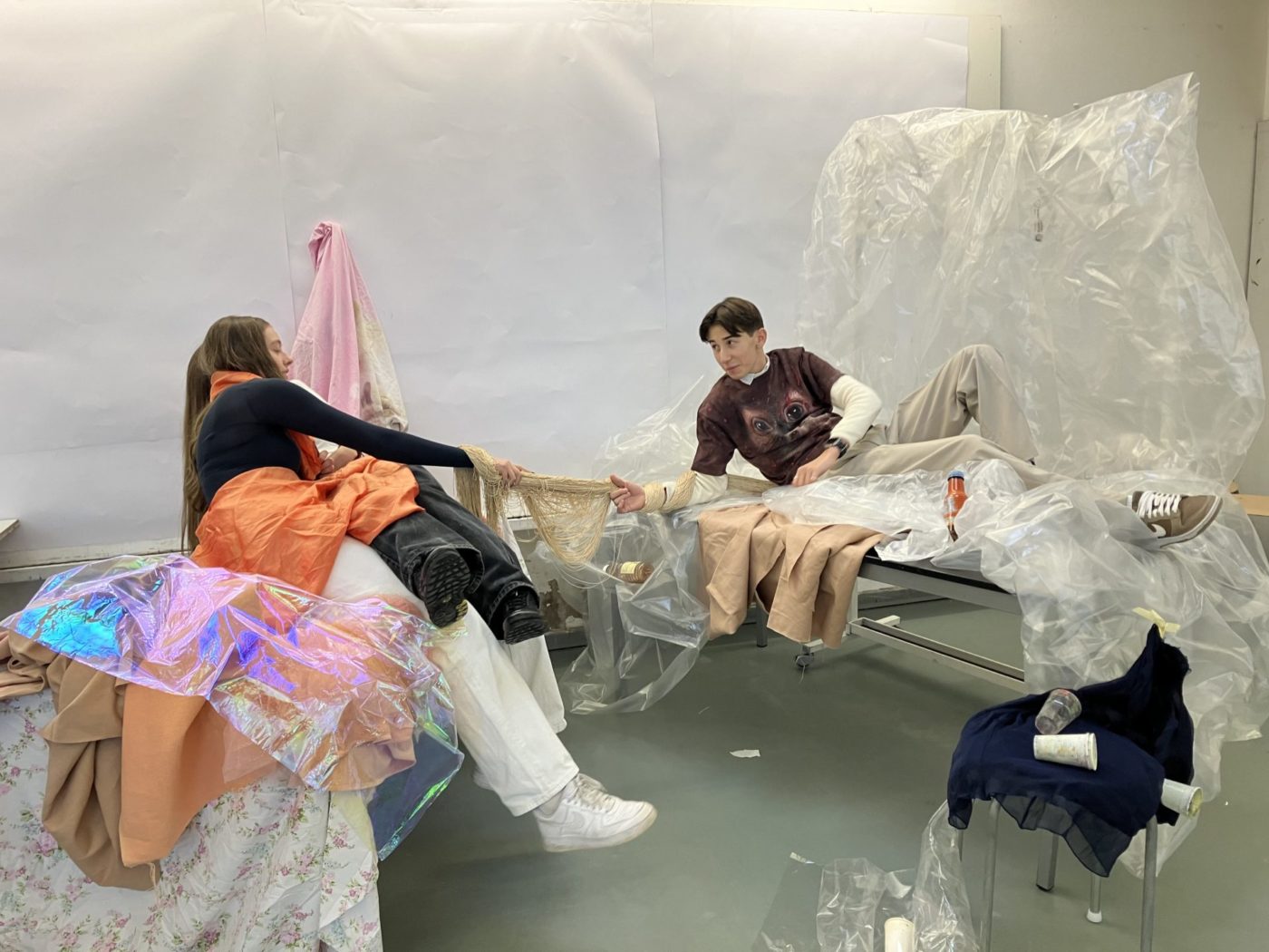 Students lie partly and are connected thanks to a net that they hold. All around them and sometimes on them, we can see coloured sheets and plastic tarpaulins.