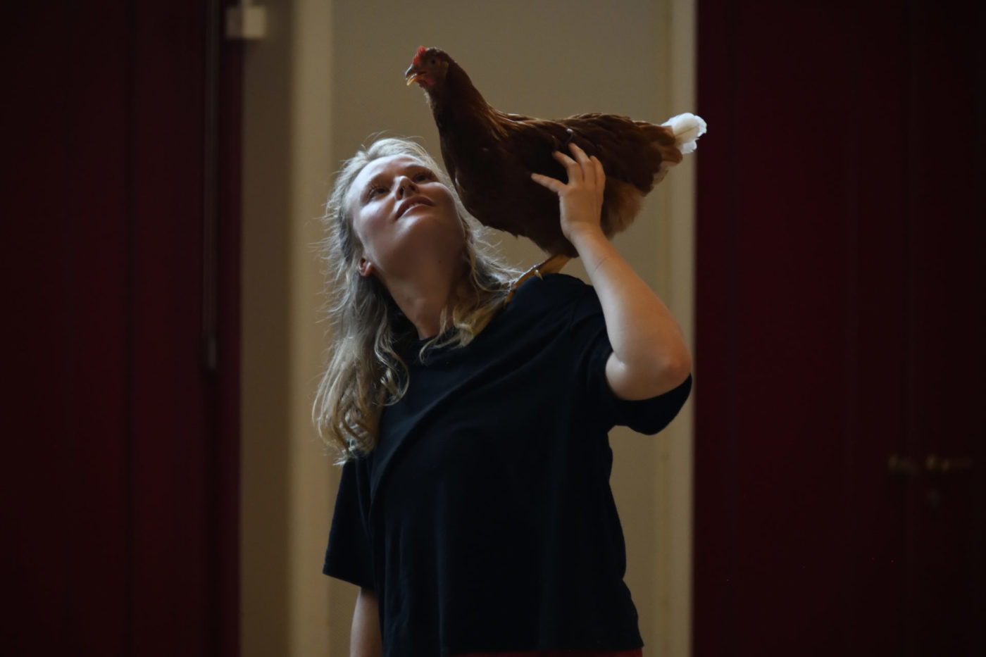 We see the artist Danae Dario holding a hen on her left shoulder. She looks at the animal.