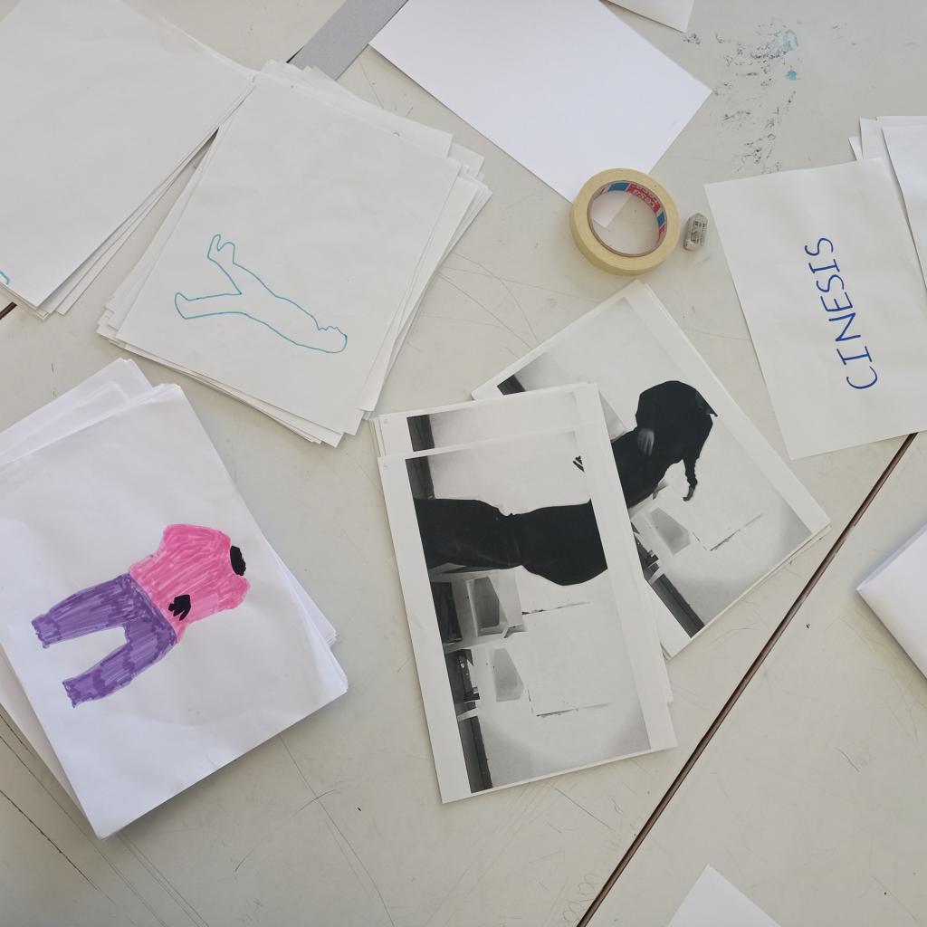 Sur une table il y a des photographies, des feuilles de papier où sont dessinées des figures ou écrits des mots pour le court-métrage ainsi que du scotch et une gomme.