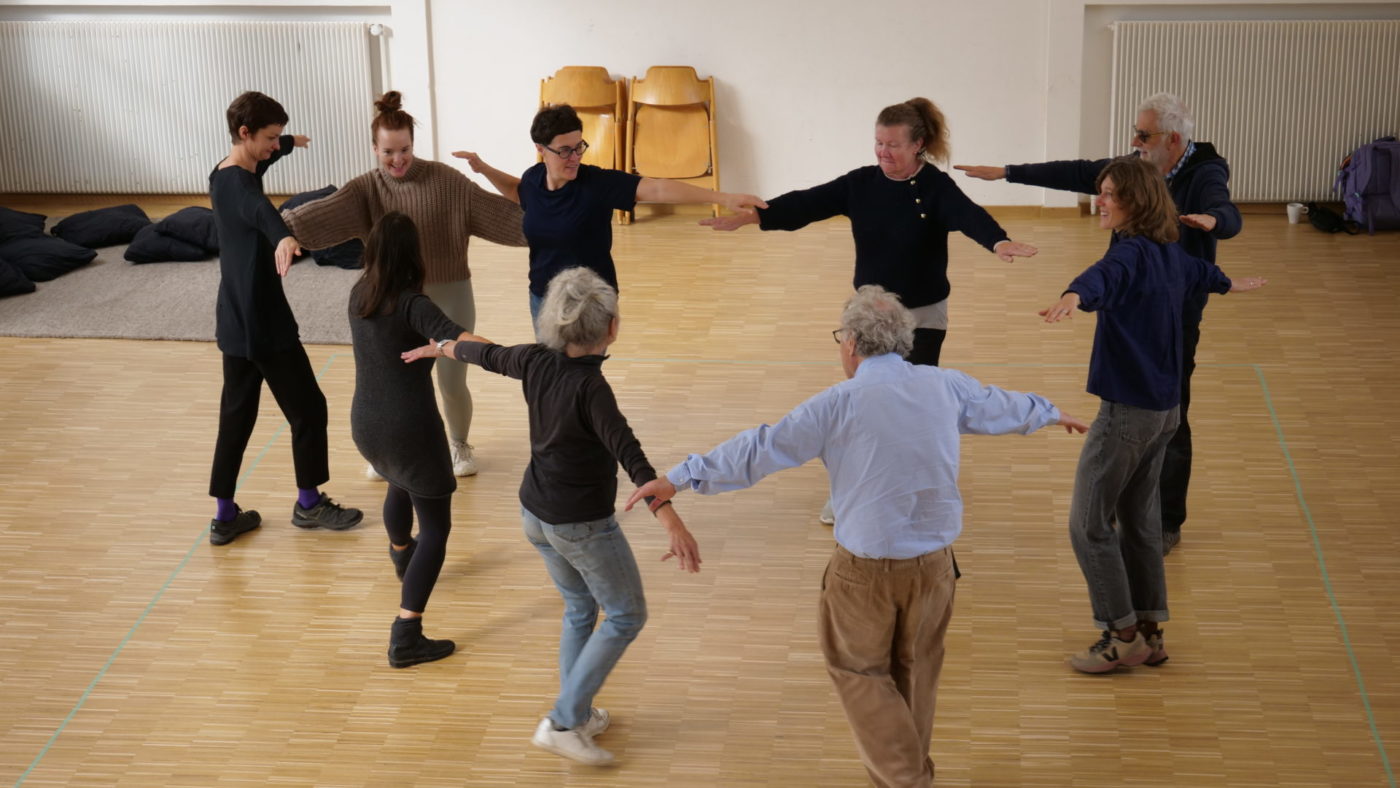 Différents participants ainsi que l'artiste Marion Thomas se tiennent debout en cercle, les bras levés comme des bras d'oiseau.