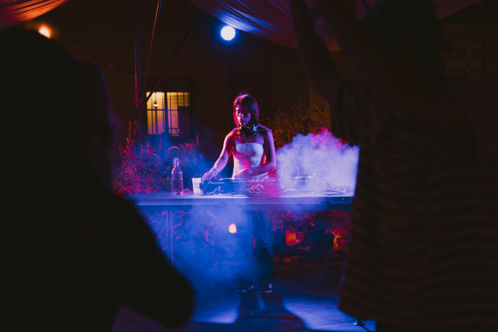 We can see the DJ ven3mo mixing sounds on a table. The lights surrounding her are purple.