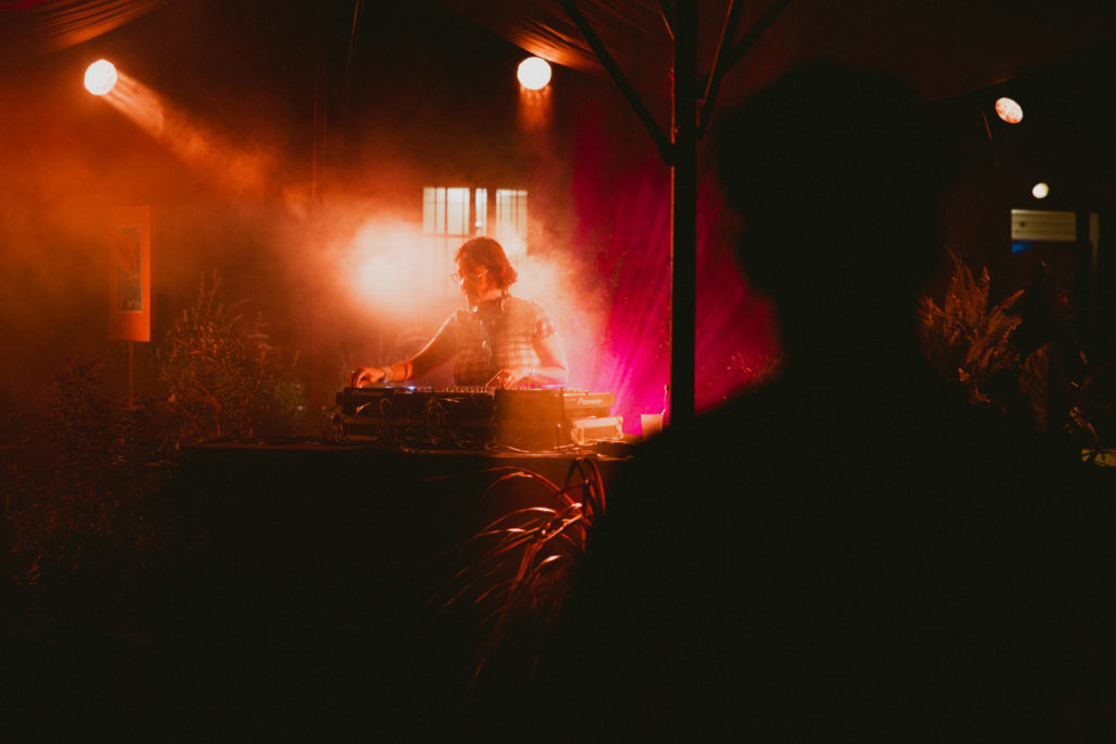 The DJette ANITA KIRPPIS mixs sounds on a table. Red and orange lights are melting in an artificial smoke.