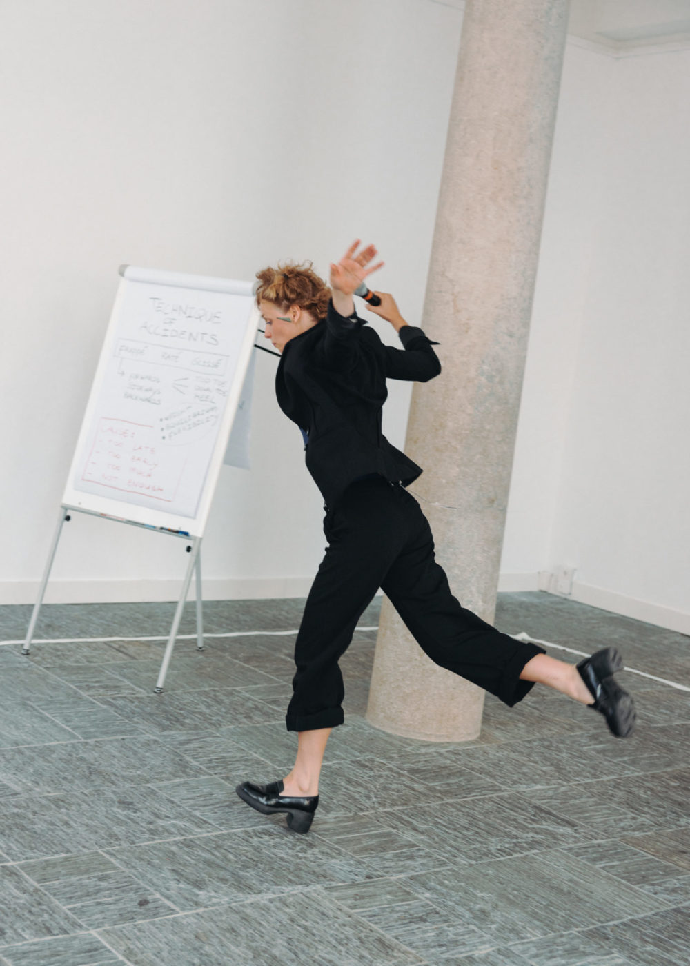 The artist Salomé Mooij wears black clothes. She has her arms in the air and experiments movements of stumble.