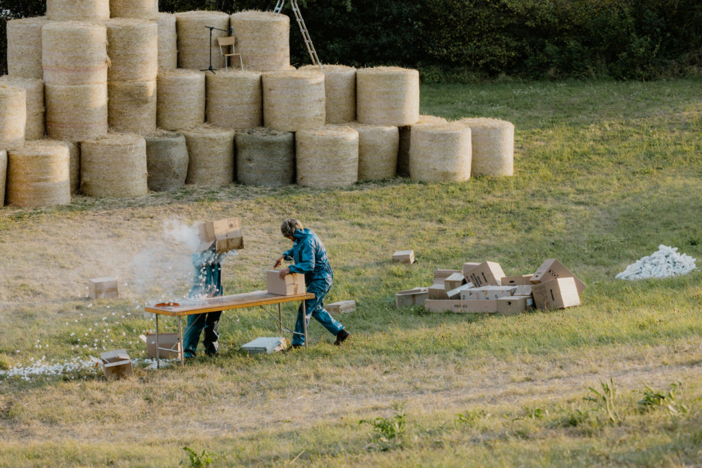 Two comedians stand on a field. In the back, we can discover a series of haystacks. One of the comedians opens a parcel and the other spills its content on his head. The content of the parcel is composed of dust and polystyrene.