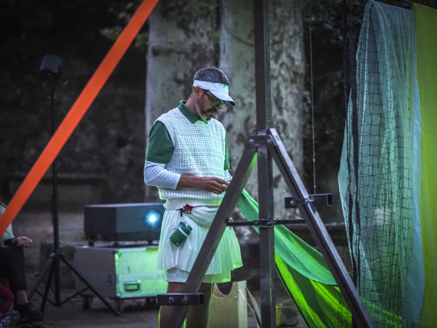 One of the actors in the play is standing; he is wearing a tennis player outfit.