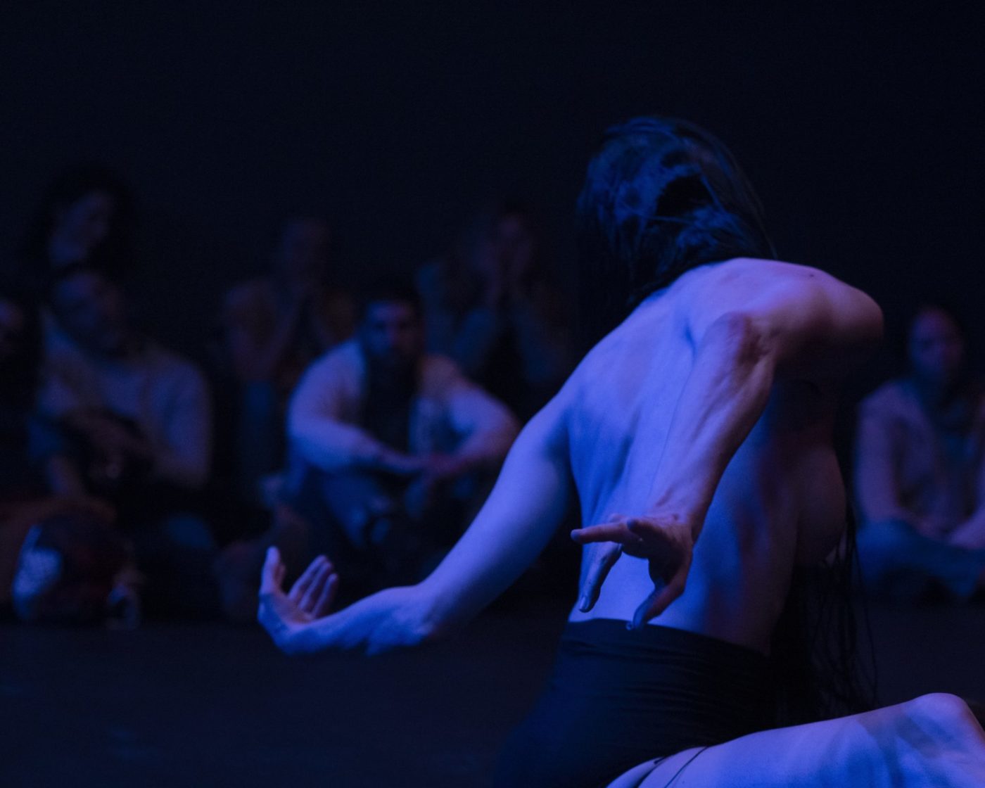 Close-up of Marion Zurbach’s back while she is dancing. Her arms are stretched backward across her back, creating a twist. The photo is dark and intriguing.