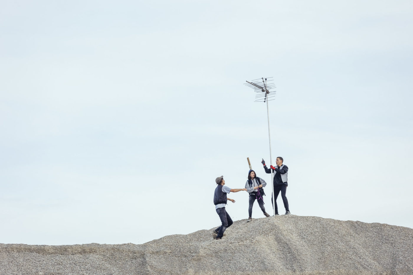 One actress and two actors are on a pile of gravel with a lightning rod. The performance takes place outdoors.