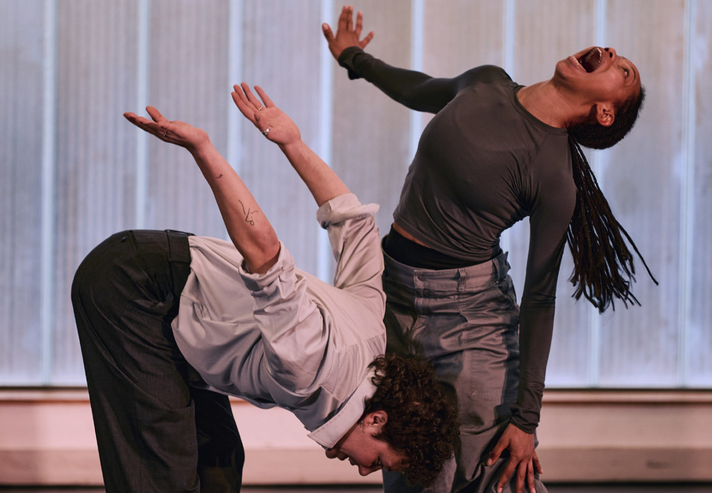 The two dancers are in motion. One woman is Black; her head is tilted back, and she seems to be shouting. The other woman is white; she is bent forward with her arms raised. The scene is intense and full of emotion.